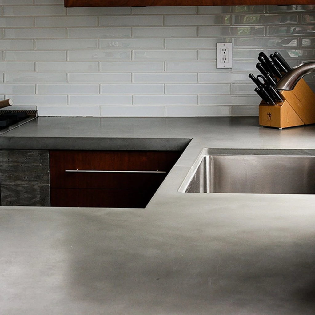 A sleek gray concrete countertop in a kitchen with subway tile walls