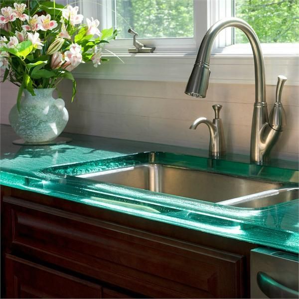 A warmly lit kitchen with green glass countertops and a big vase of flowers