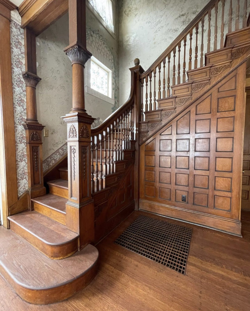 The front hallway and stairs -- beautifully carved medium brown wood, with decorative columns and banister.