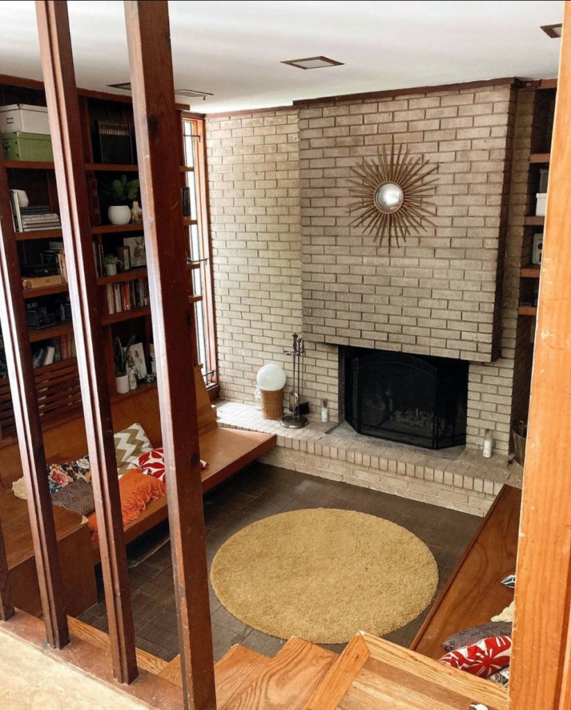 The living room of a renovated mid century modern house, with an imposing gray brick fireplace and a retro sunburst decoration.