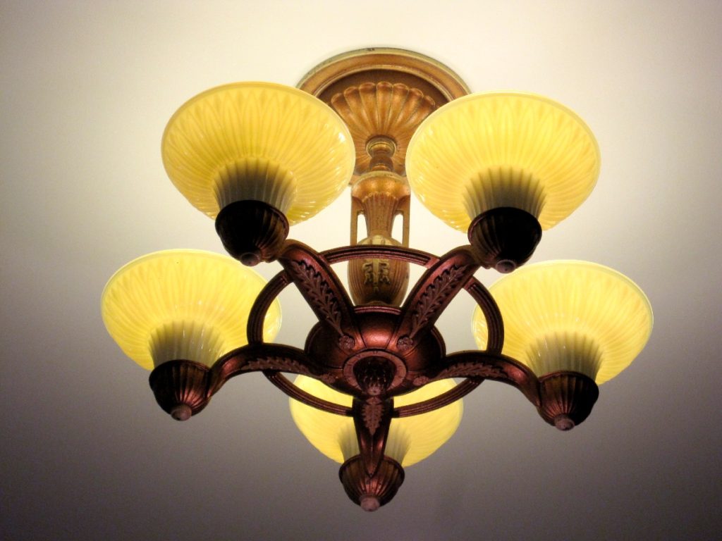 A view from below of an antique chandelier style lighting fixture with yellow glass sconces.