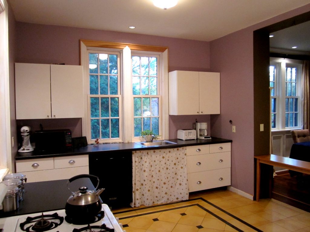 A kitchen before a renovation, with purple walls and dated cabinets.