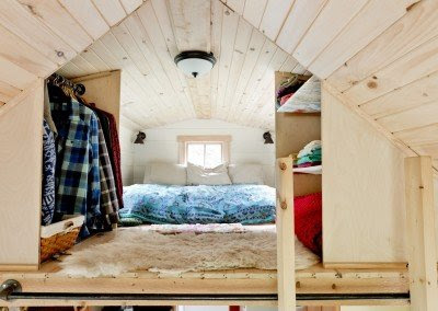 The lofted sleeping area of the tiny house, paneled with light wood, under the gable.