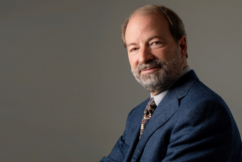 A professional headshot of Donald Rattner, a light-skinned man with balding brown hair and a close-cropped brown-and-gray beard. He is wearing a suit and tie, and looking warmly at the camera.