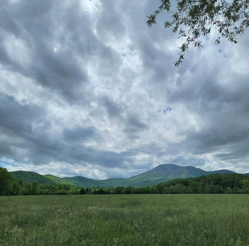 A view of a meadow outside the Blue Ridge Mountains with dramatic clouds sweeping overhead