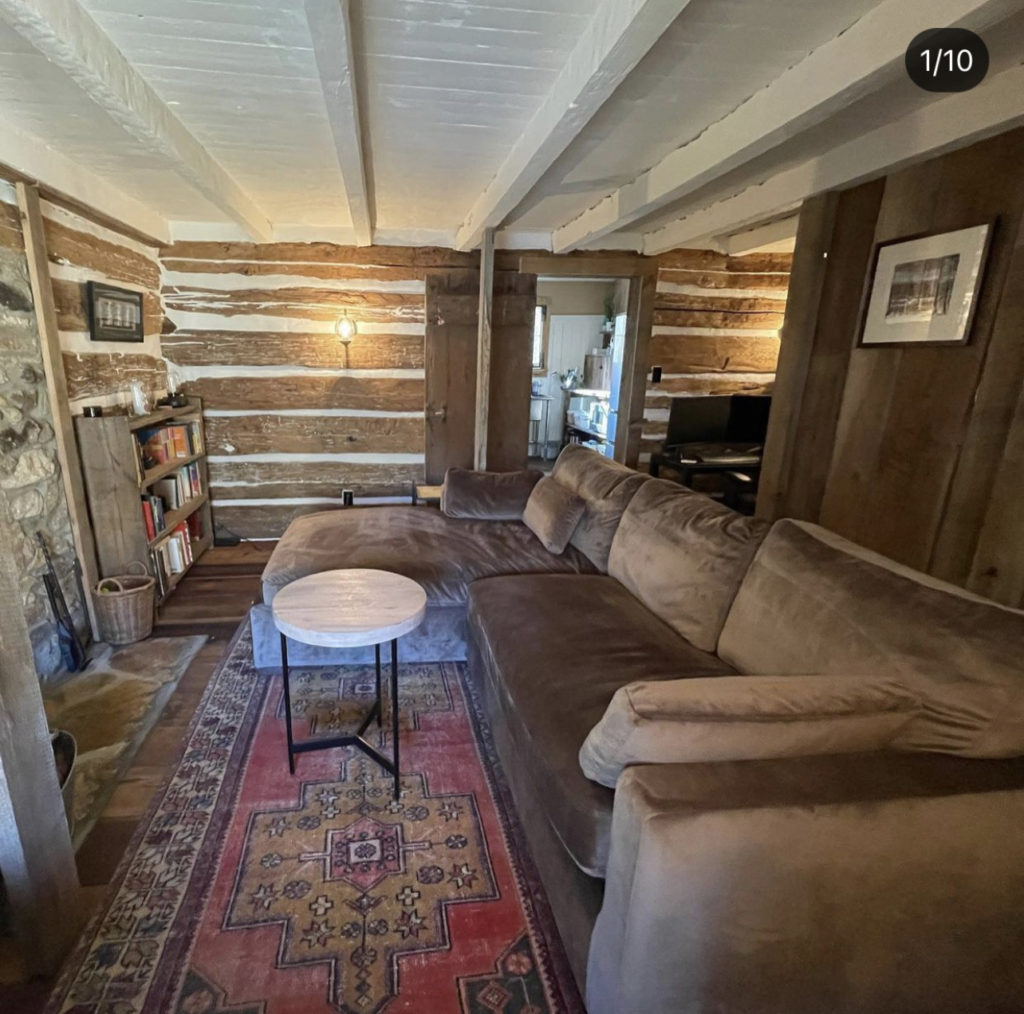 The living room of the log cabin after renovation, with a vintage Persian rug, brown couch, and rustic decor.