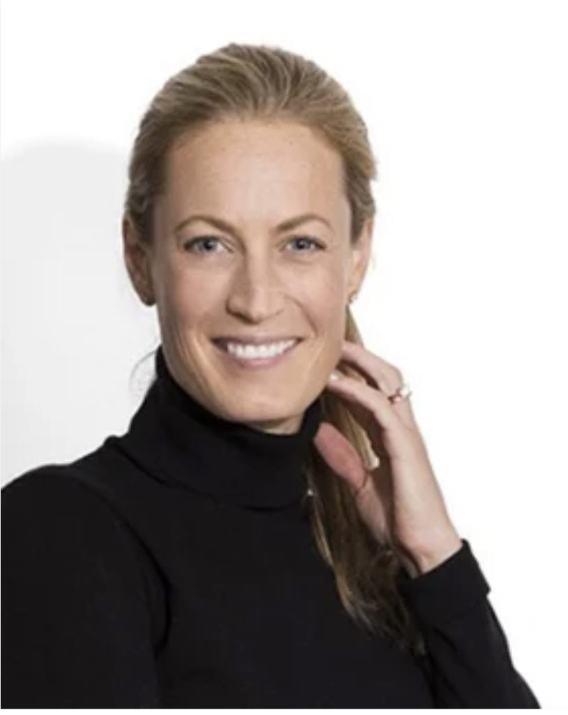 A headshot of Christine Williamson smiling. She has light skin and light brown hair in a ponytail, and is wearing a black turtleneck.