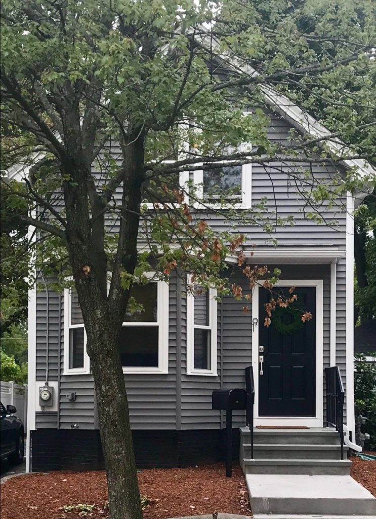 The finished house with new gray siding, white trim, and a black door. 