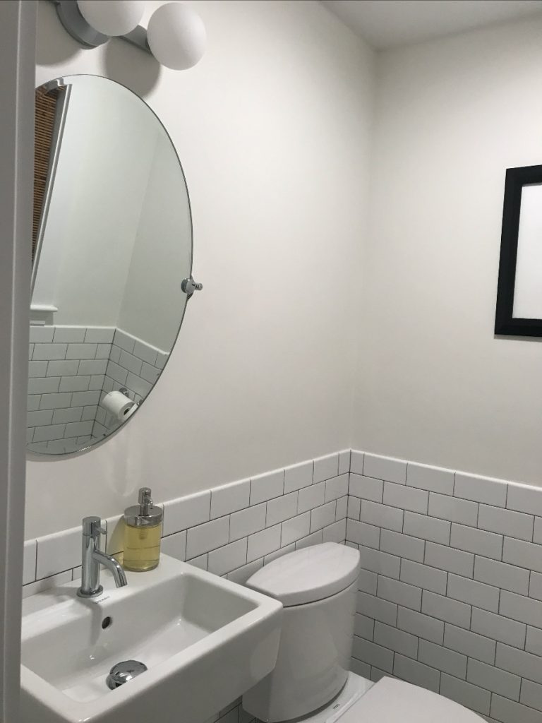 A newly renovated bathroom with white subway tile, a square sink, and a trendy round adjustable mirror.