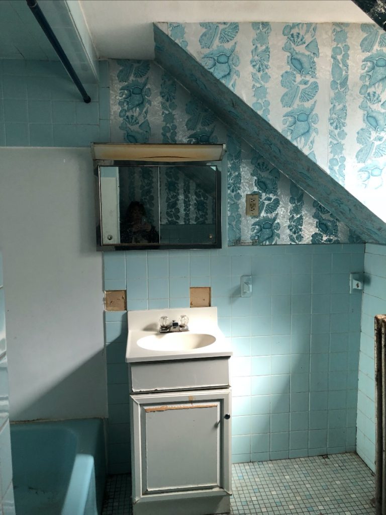 A bathroom with blue tile and blue seashell wallpaper.