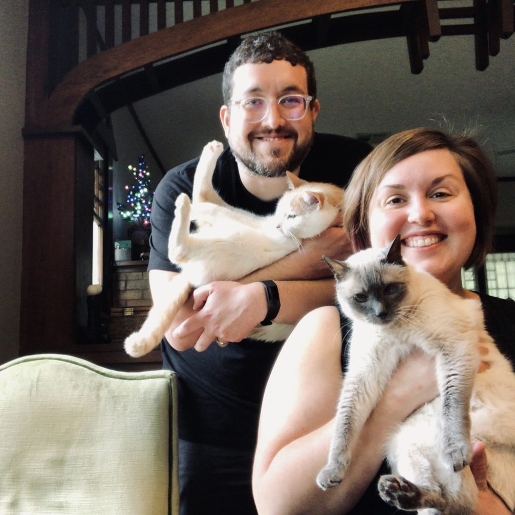 Katelyn and Brian smiling for a photo with their cats in the bungalow.