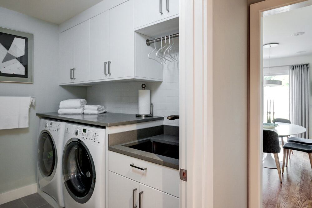 A photo of a new-looking laundry room. All the cabinets and tile are white. 