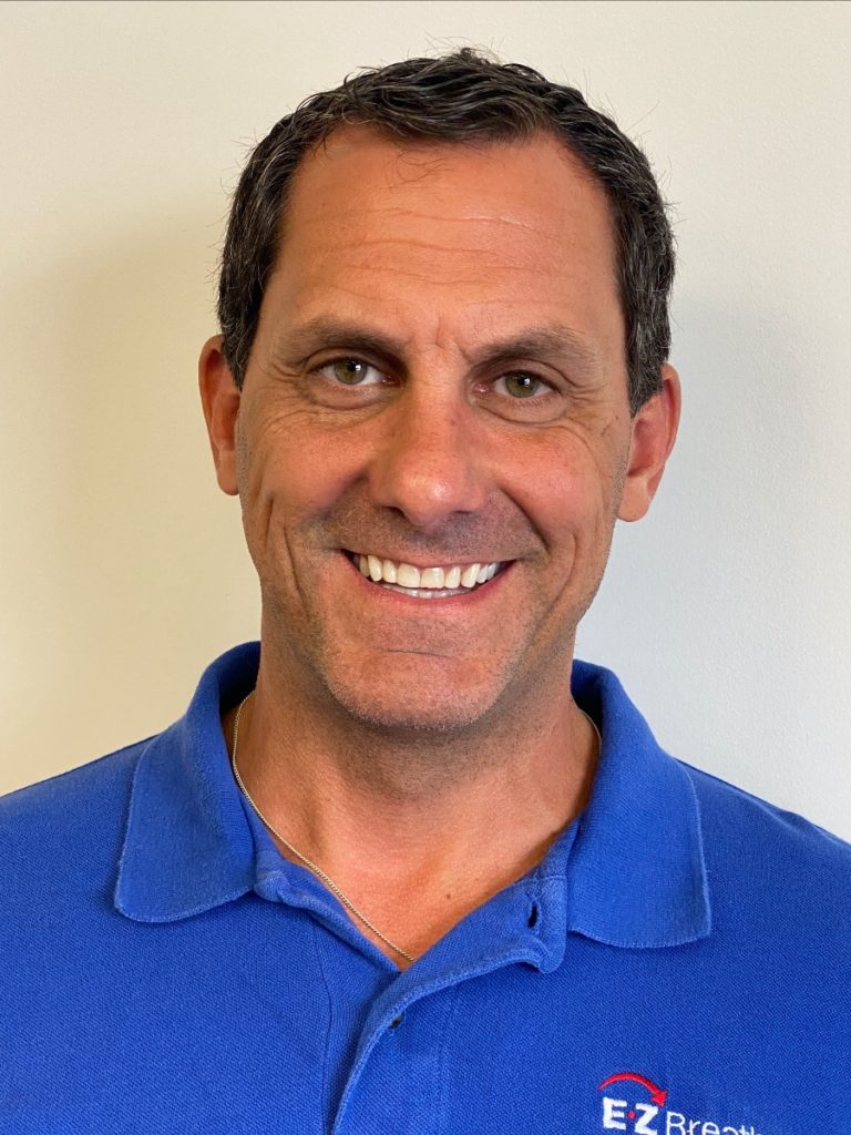 A headshot photo of Andre LaCroix, a light-skinned man with brown eyes and short, dark hair. He is smiling at the camera, which makes the corners of his eyes crinkle up. He's wearing a blue EZ Breathe branded polo shirt.