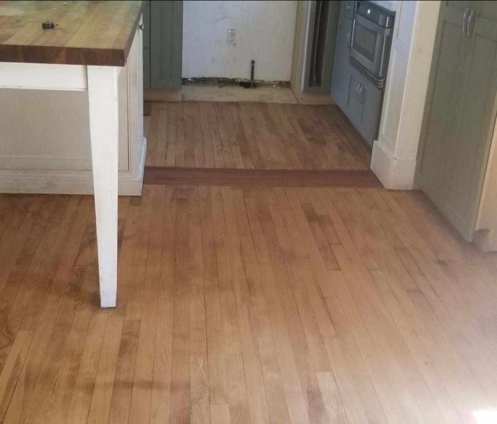 A hardwood floor during restoration. It's been sanded. There is light staining, but most of the wear and damage is gone.