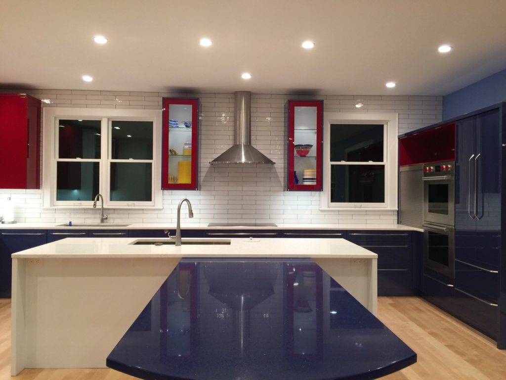 The kitchen after renovation. it has white subway tile and a quartz countertop with modern sink, and glossy blue and red surfaces all around.