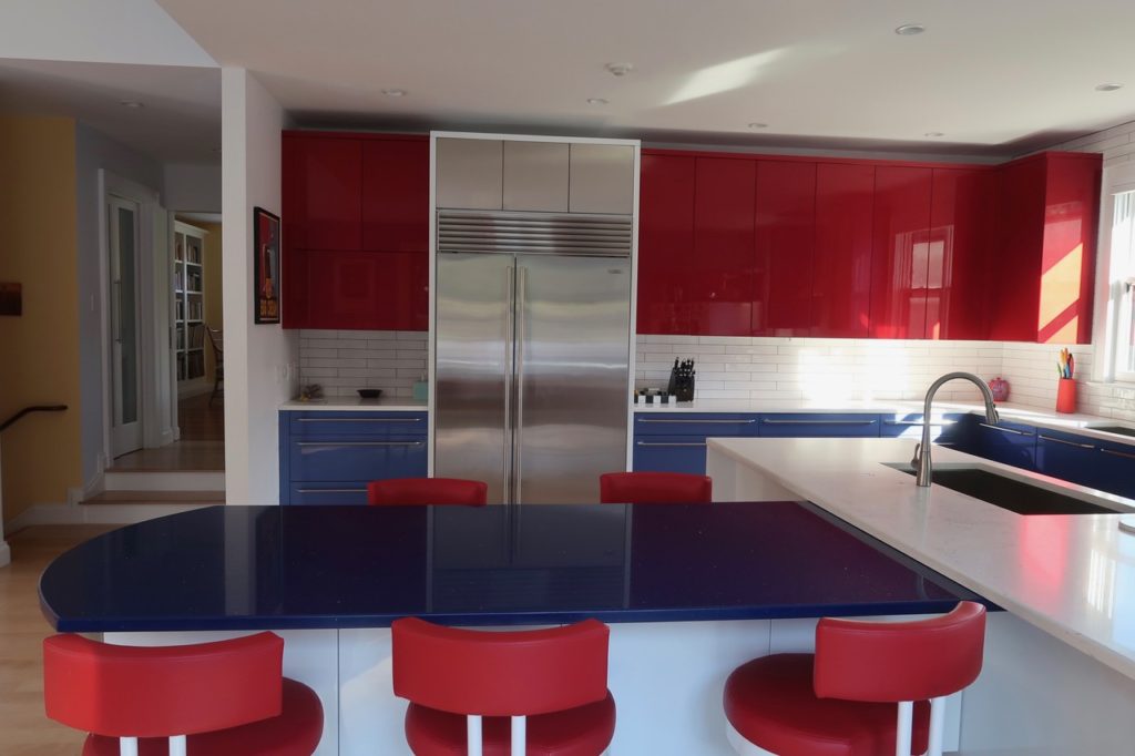 A view of the kitchen's chrome fridge, shiny red cabinets, and minimalist red swivel chairs.