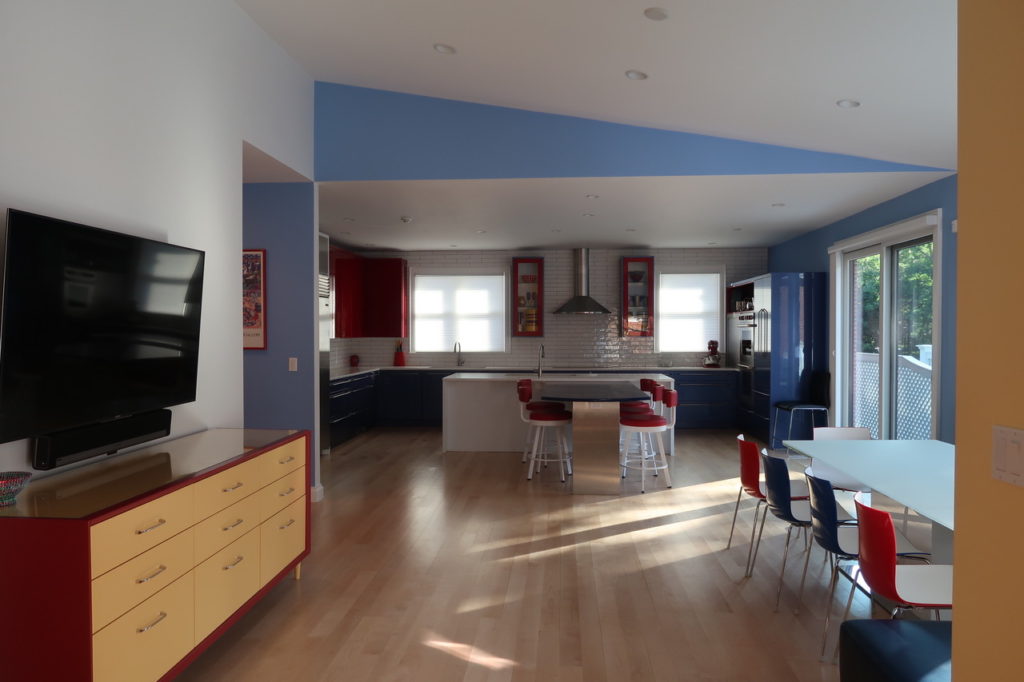 A view of the kitchen from the dining room. A glossy red TV console complements the red chairs and cabinets.