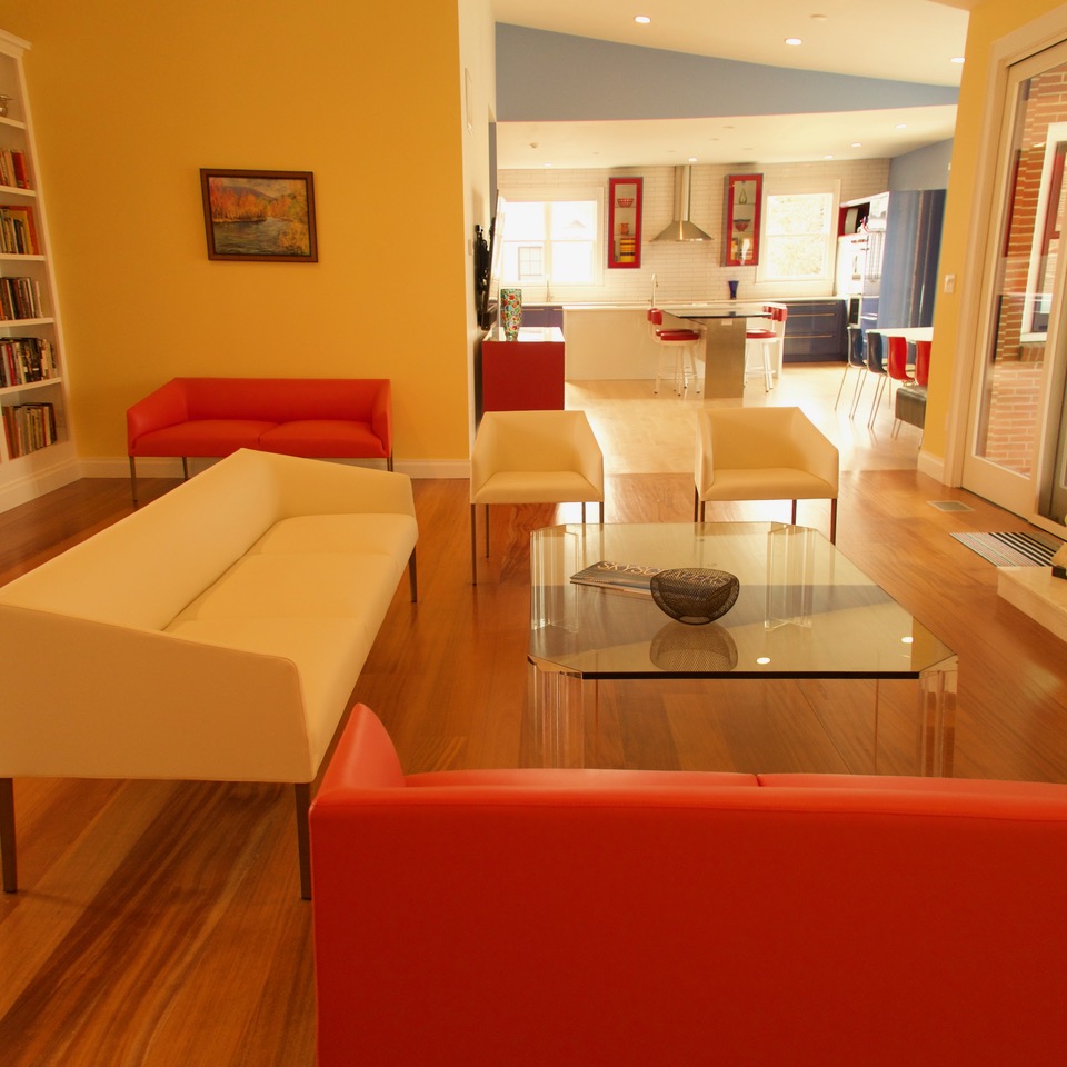 A view of the living room with sleek, geometric-looking red and white couches and a glass coffee table. The kitchen is visible through the open plan in the background.