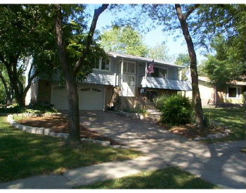 A split level house before renovation. There is a garage on the right and overhangs between the first and second stories on both sides.