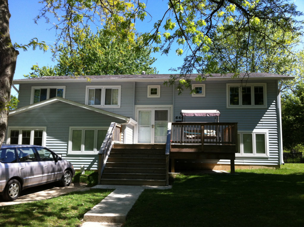 The split level house after renovation. The garage has been replaced by an addition with a slightly gabled roof, and there is now a deck on the right side.