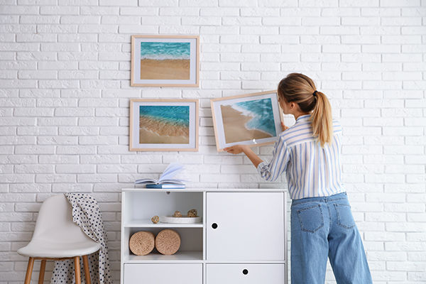 A woman putting up framed photographs of the ocean in her modern house