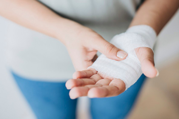 A stock photo of a person touching their injured hand, which has a gauze bandage on it.