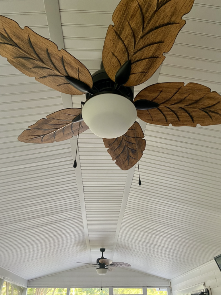 A close-up of a ceiling fan in a screened porch. The blades of the fan look like wooden palm tree leaves.