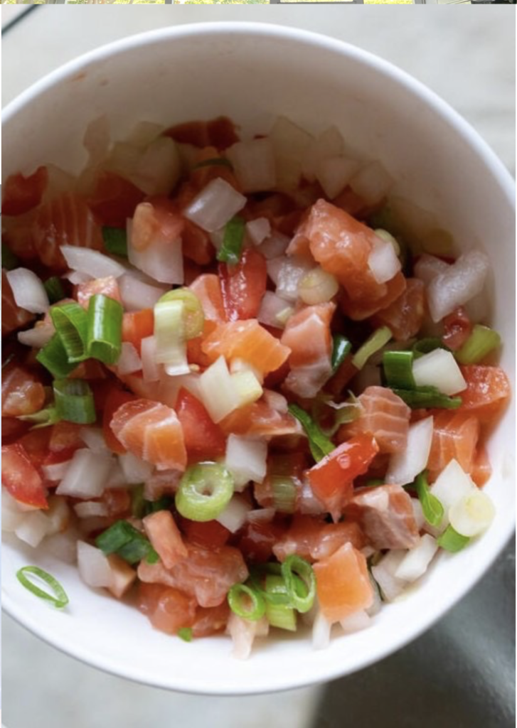 A close-up of a diced salad with raw salmon, scallions, tomatoes, and regular onions.