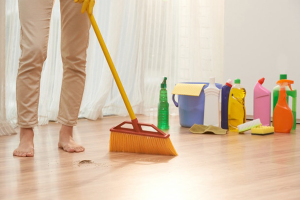 A person from the waist down, sweeping the floor with a bunch of cleaning products behind them.