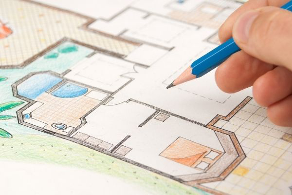 A close-up of an architect's hand working on an architectural drawing with a blue pencil.