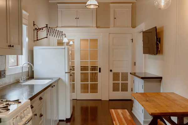 A restored kitchen in a historic home. It has a timeless white design. There are French doors and a telescoping light.