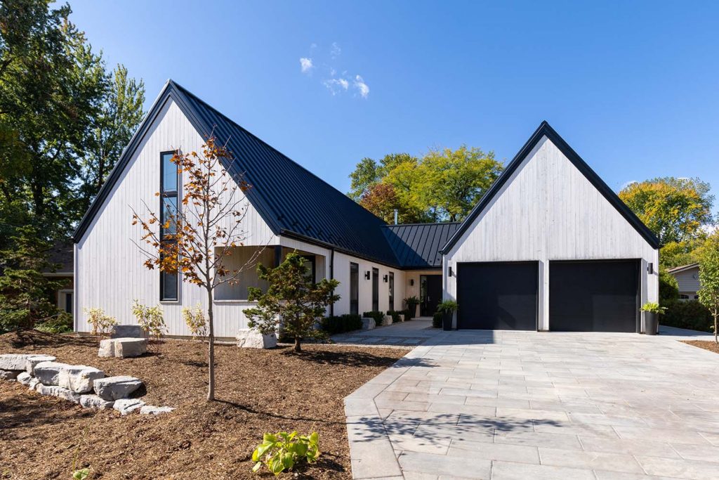 A house and garage designed by architect Dory Azar. The buildings have a clean, modern design, with sharply pointed black roof gables over white vertical siding.