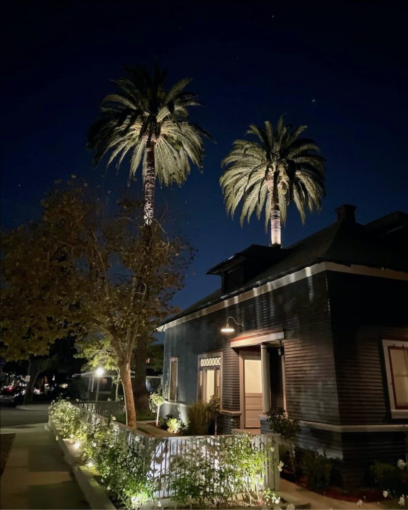 One of Hugh's historic home restoration projects at night: a small, cute one story house with two palm trees behind it.